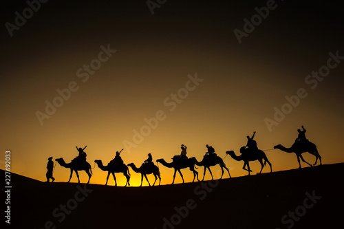 Sillhouette of camel caravan with happy peopple going through the desert at sunset with blue and red sky photo