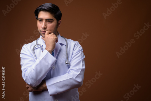 Young handsome Iranian man doctor against brown background