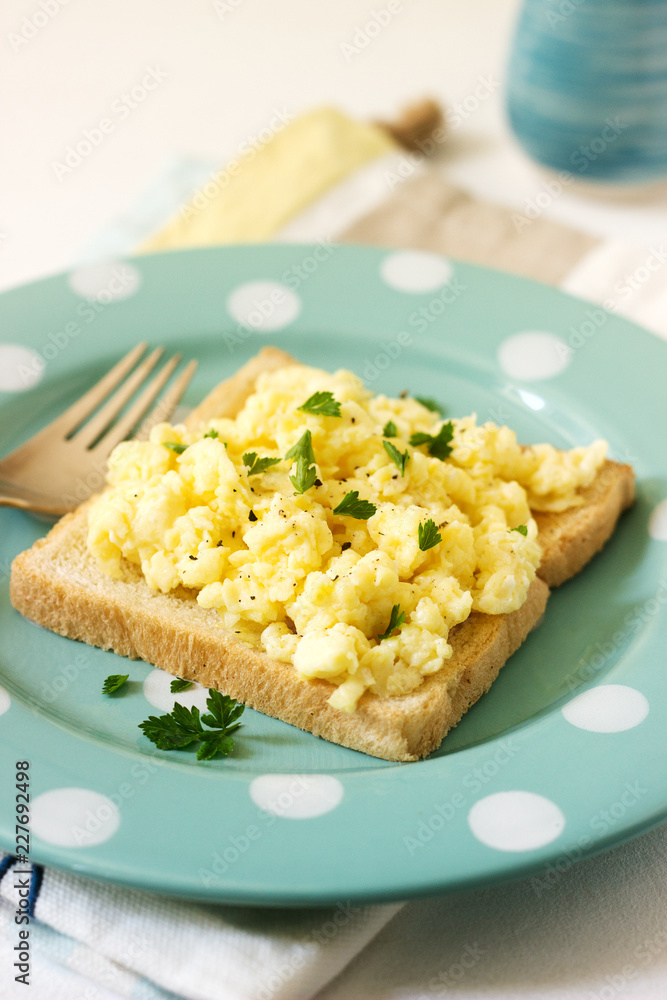 Simple classic breakfast of bread toast and scrambled eggs with parsley.