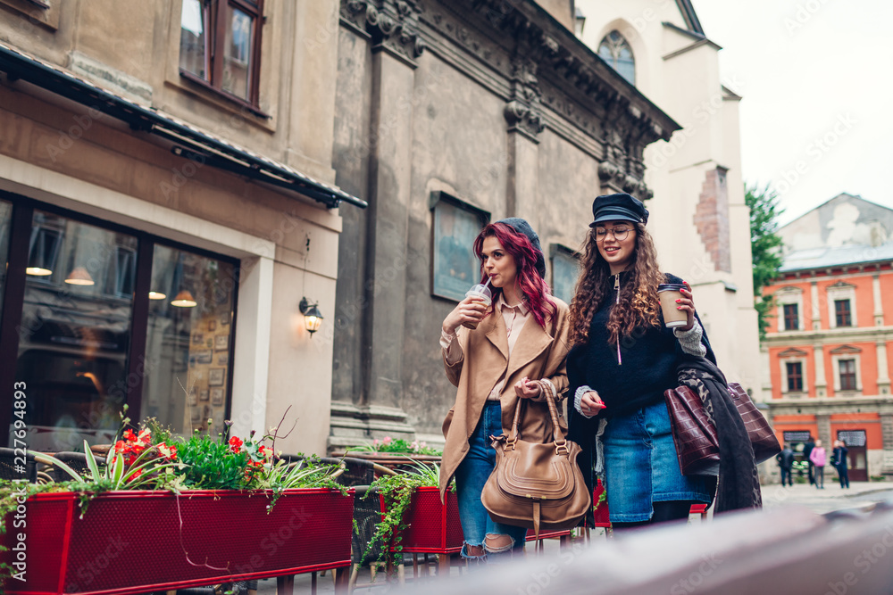 Obraz premium Outdoor shot of young women walking on city street. and having coffee. Friends talking and having fun
