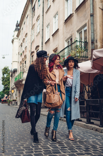 Outdoor shot of three young women walking on city street. Girls talking and hugging