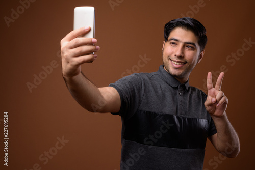 Studio shot of young handsome Iranian man against brown backgrou