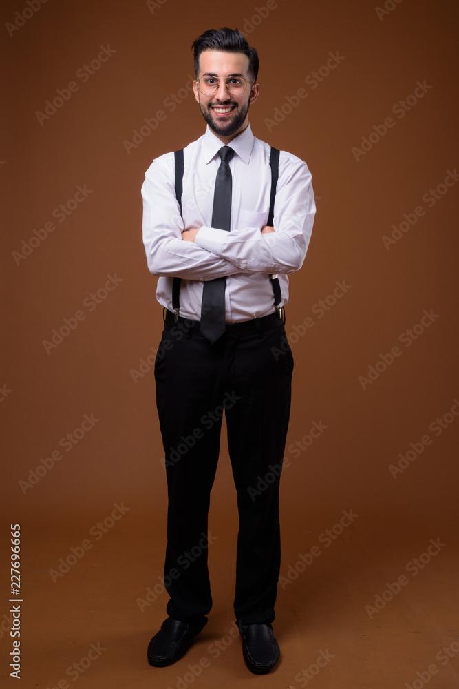 Young handsome bearded Iranian businessman against brown backgro Young handsome bearded Iranian businessman against brown backgro