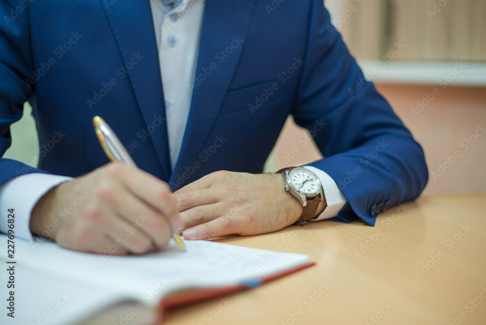 businessman in a suit signs the paper, man holding a pen, a man sits at the table and writes businessman in a suit signs the paper, man holding a pen, a man sits at the table and writes