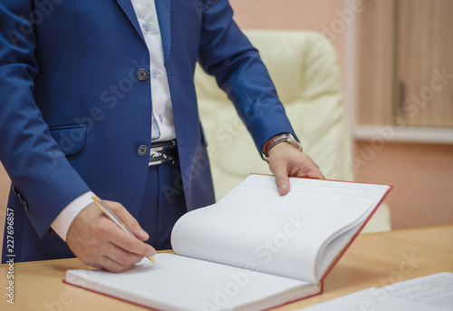 man in suit writing on a Notepad, the man signs the documents