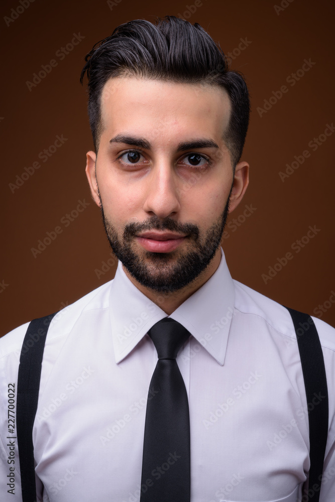 Young handsome bearded Iranian businessman against brown backgro Young handsome bearded Iranian businessman against brown backgro