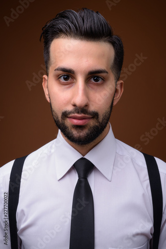 Young handsome bearded Iranian businessman against brown backgro