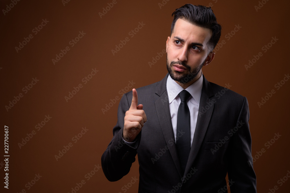 Young handsome bearded Iranian businessman against brown backgro Young handsome bearded Iranian businessman against brown backgro
