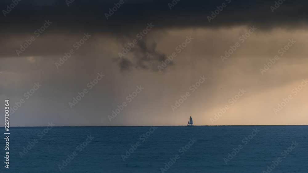 A yacht far out to sea about to sail into rain.