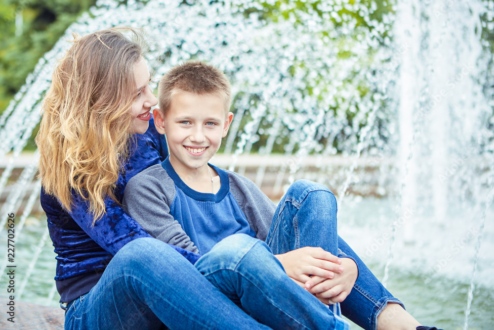 Fototapeta premium Happy beautiful mother and son enjoying near the fountain