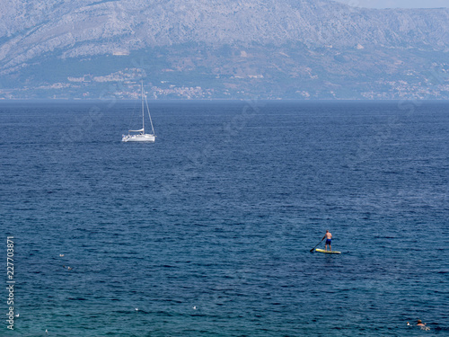 Coastline at Adriatic sea, Croatia. A swimmer, a man on a paddling board and sailing boat at the sea. Sunny summer day.