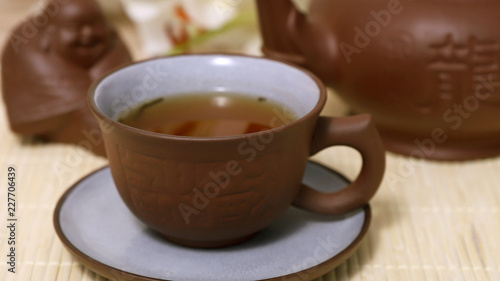 Зеленый чай в керамической чашке и чайнике, будда и цветок