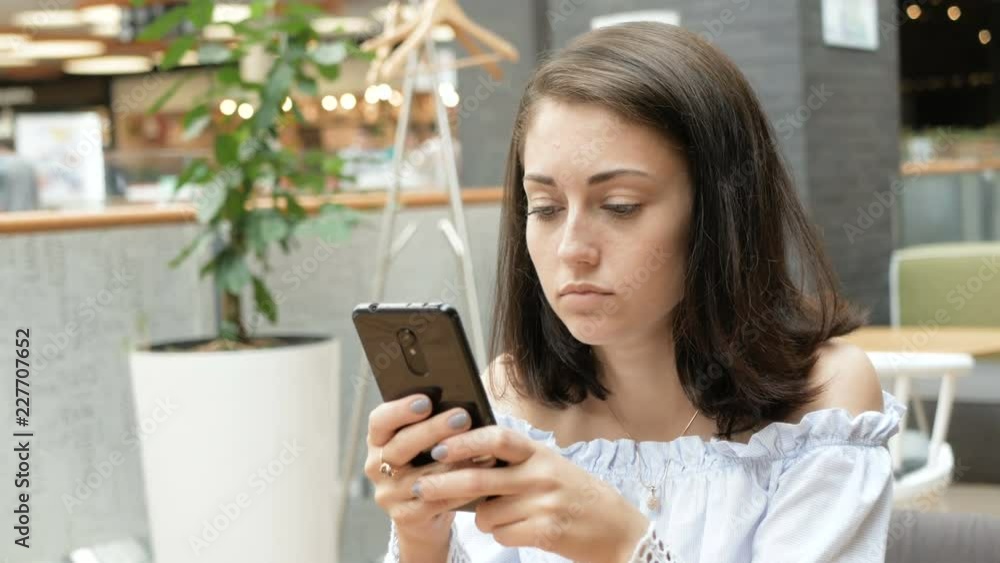Portrait of pretty dreamy young woman with smartphone in hand at table in cafe. Food court mall. close-up Portrait of pretty dreamy young woman with smartphone in hand at table in cafe. Food court mall. close-up