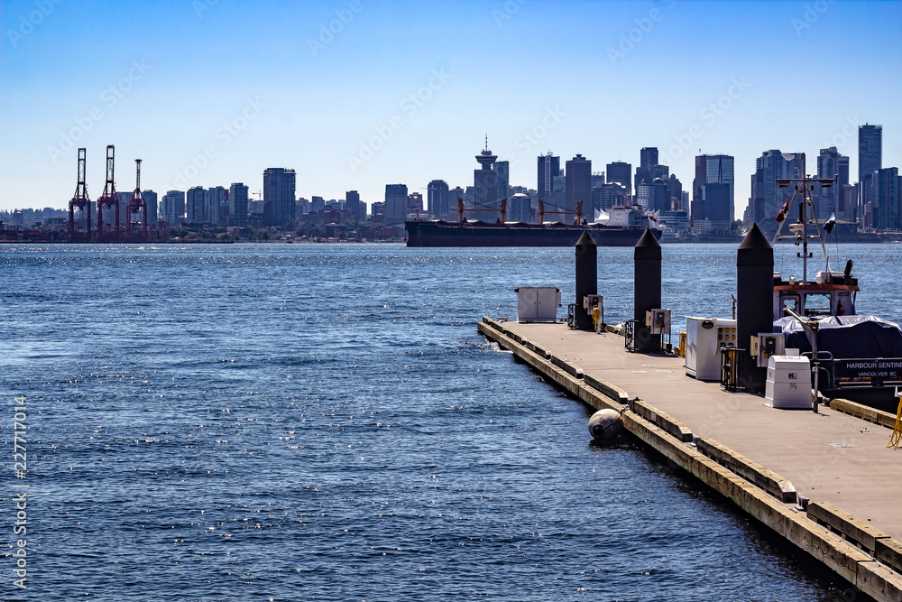 Looking off the dock at Lonsdale Quay, Vancouver British Columbia on a sunny day at a major shipping lane. Barges, tugs and city skyline
