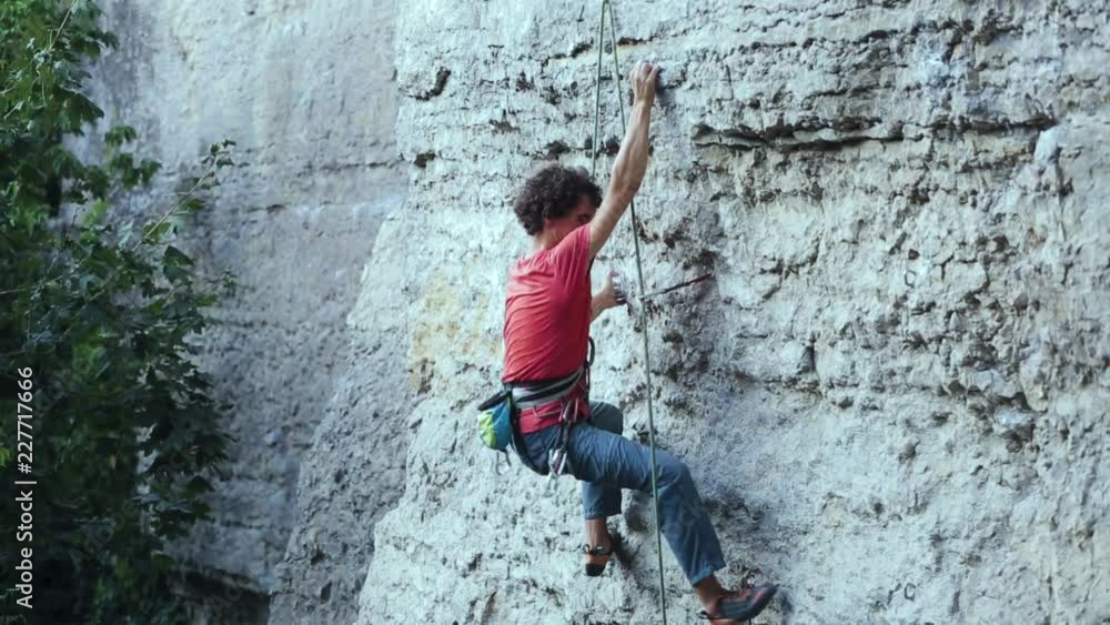 back side view of young man rock climber in bright blue pants climbing on the cliff. man making hard move on the challenging route back side view of young man rock climber in bright blue pants climbing on the cliff. man making hard move on the challenging route