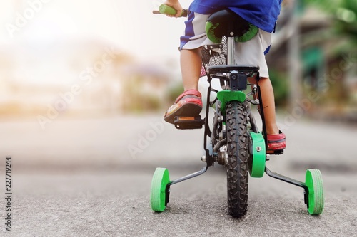 Learning to ride a bike concept, The little boy is practicing cycling a bicycle with the training wheels on the road.