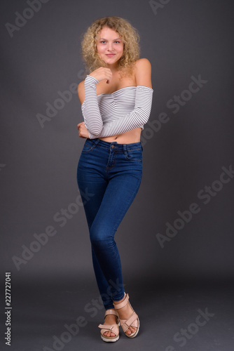 Young beautiful woman with blond curly hair against gray backgro