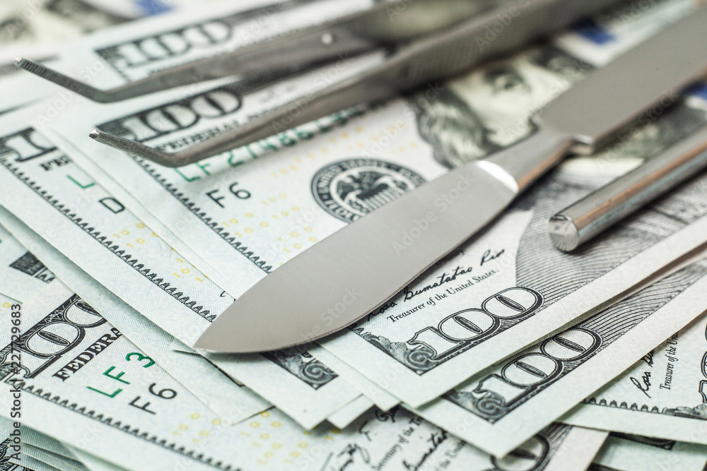 Scalpel and tweezers on pile of cash bills dollars. Concept expensive surgery, medical insurance Scalpel and tweezers on pile of cash bills dollars. Concept expensive surgery, medical insurance
