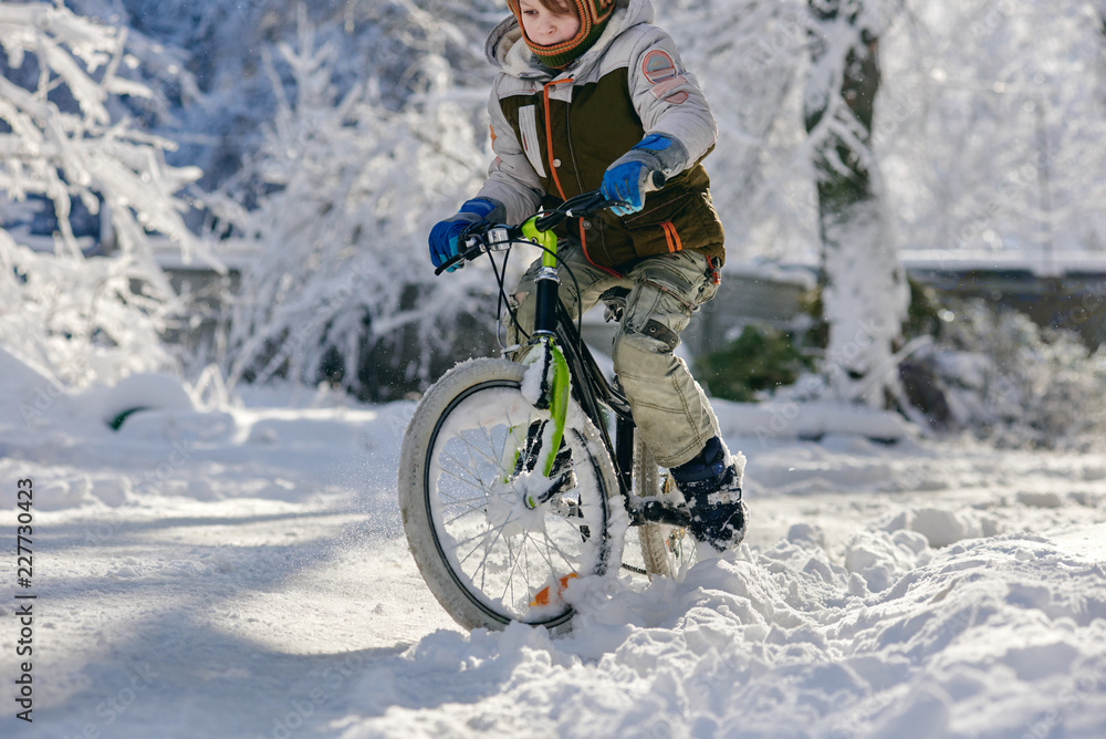 Little boy riding bicycle on snowy winter road