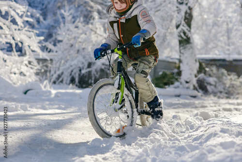 Little boy riding bicycle on snowy winter road