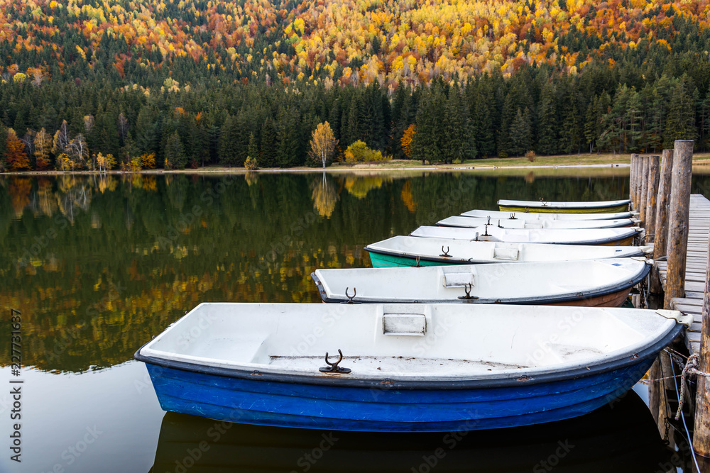 Boats at lakeside, beautiful unique vulcanic lake at autumn, ( Lake Saint Ana) deciduous  colorful woods mixed with pine woods reflecting on the crystal clean water in Transylvania , Romania.
