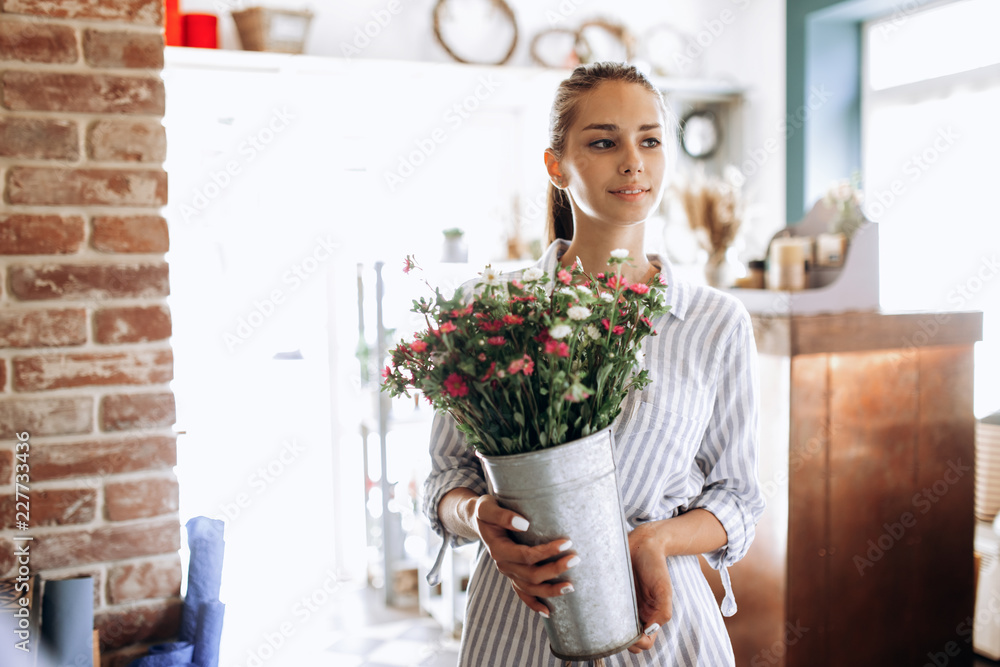 Beautiful brunette girl dressed in a striped dress holds a vase with pink and white chrysanthemums in the flower shop