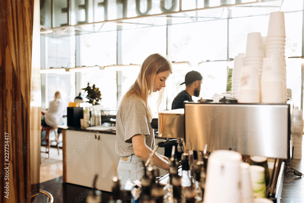 A young pretty thin blonde with long hair,dressed in casual outfit,is cooking coffee in a modern coffee shop. A young pretty thin blonde with long hair,dressed in casual outfit,is cooking coffee in a modern coffee shop.