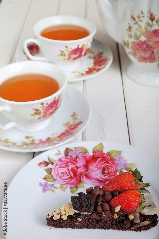 Piece of delicious homemade brownie cake with strawberries and tea set on white table. Selective focus Piece of delicious homemade brownie cake with strawberries and tea set on white table. Selective focus