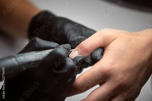 Finger nail treatment, fashion, manicure making process in beauty salon Electric nail file drill in action, close up of beautician hands in black gloves working on client fingernails.