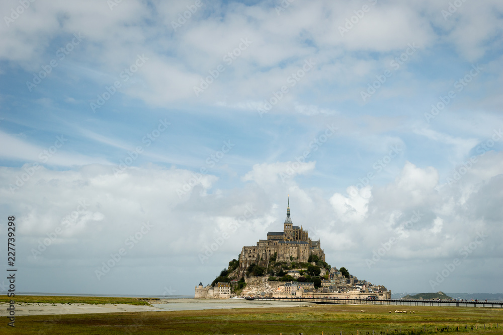 Beautiful view of famous historic Le Mont Saint-Michel abbey tidal island on fields of fresh green grass on a sunny day with blue sky and clouds in summer, Normandy, northern France