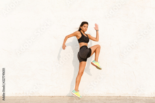 Full length image of energetic woman 20s in sportswear working out and running, along wall
