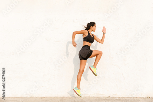 Full length image of young sportswoman 20s in sportswear working out and running, along wall