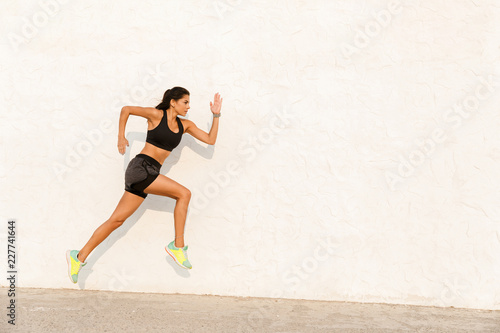Full length image of caucasian woman 20s in sportswear working out and running, along wall