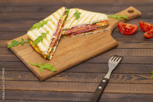 Grilled sandwiches with ham, cheese, tomatoes and arugula salad on a dark background. Delicious breakfast.