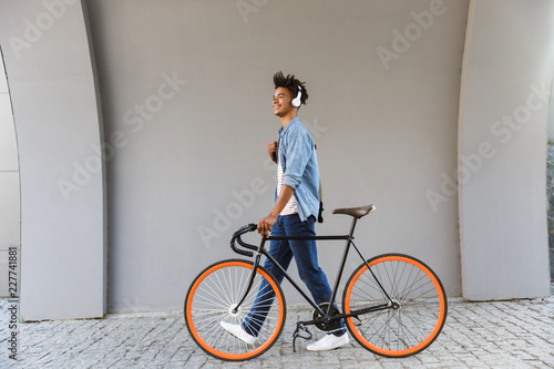 Smiling young african man outdoors, walking with bicycle photo