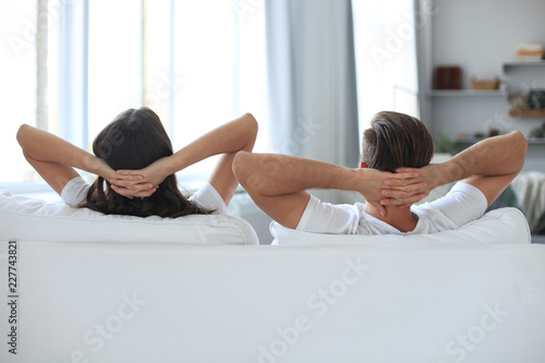 Rear view of a couple relaxing on a sofa at home and looking forward. photo