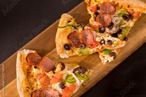 Slices of traditional pizza with sausage, maushrooms, peppers, tomato, olives, cheese and onion on a wooden board isolates on a black background photo