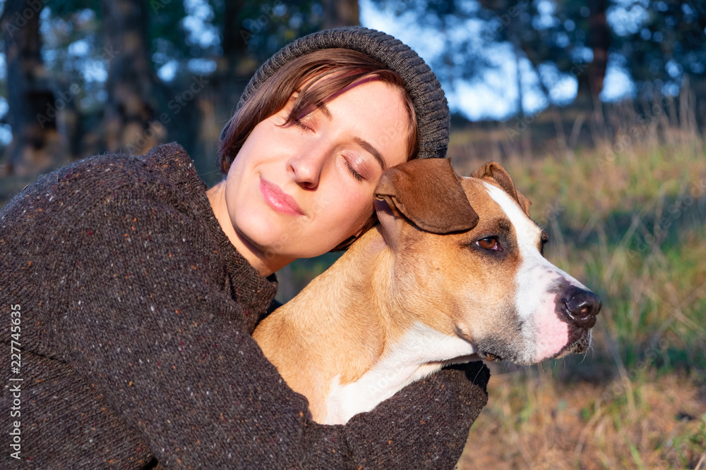 Hugging a dog in beautiful nature at sunset. Woman facing evening sun sits with her pet next to her Hugging a dog in beautiful nature at sunset. Woman facing evening sun sits with her pet next to her