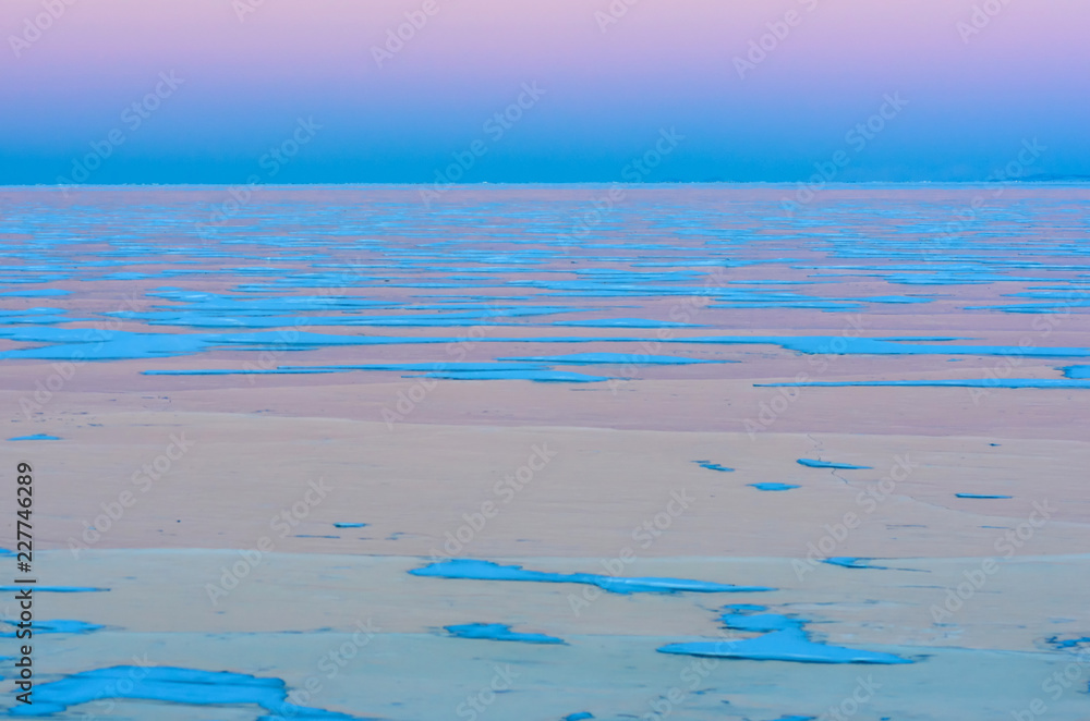 Obraz premium Blue ice of Baikal lake under pink sunset sky
