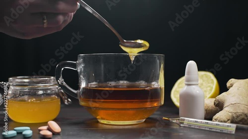 Honey is added to the glass vup with black tea, lemon tea and honey stands on the table with pills and thermometer, natural treatment against illness and sickness, catch a cold, immunity uplift photo