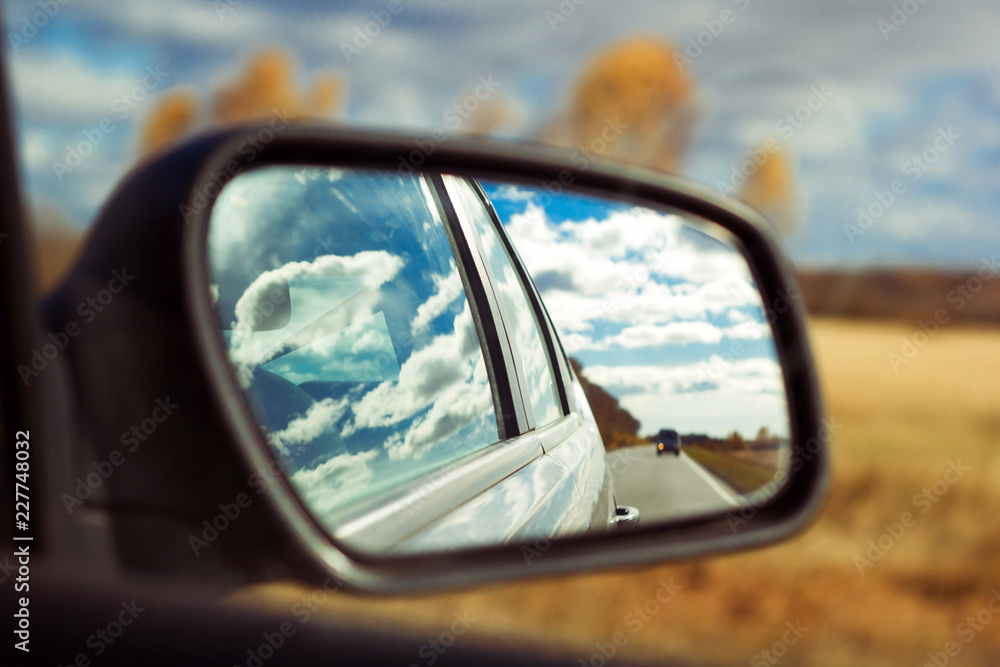 blue sky with fluffy clouds and road reflection an car mirror on a background of autumn field