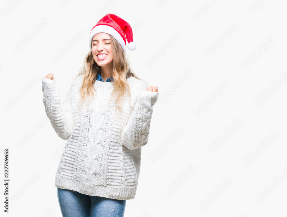 Beautiful young blonde woman wearing christmas hat over isolated background very happy and excited doing winner gesture with arms raised, smiling and screaming for success. Celebration concept. Beautiful young blonde woman wearing christmas hat over isolated background very happy and excited doing winner gesture with arms raised, smiling and screaming for success. Celebration concept.