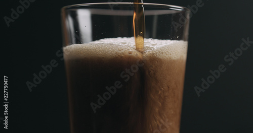 Closeup pour dark stout beer in pint glass over black background