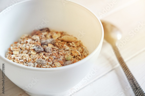 healthy breakfast muesli with snacks, white bowl and spoon on white wood background