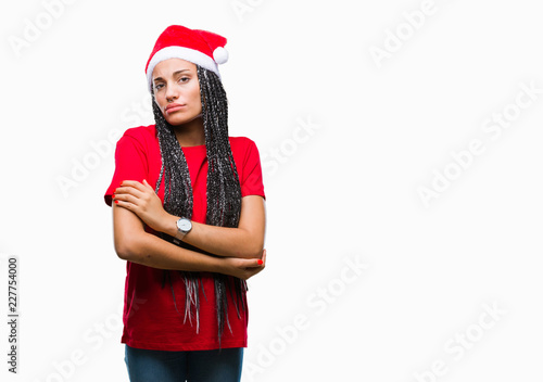 Young braided hair african american girl wearing christmas hat over isolated background skeptic and nervous, disapproving expression on face with crossed arms. Negative person.