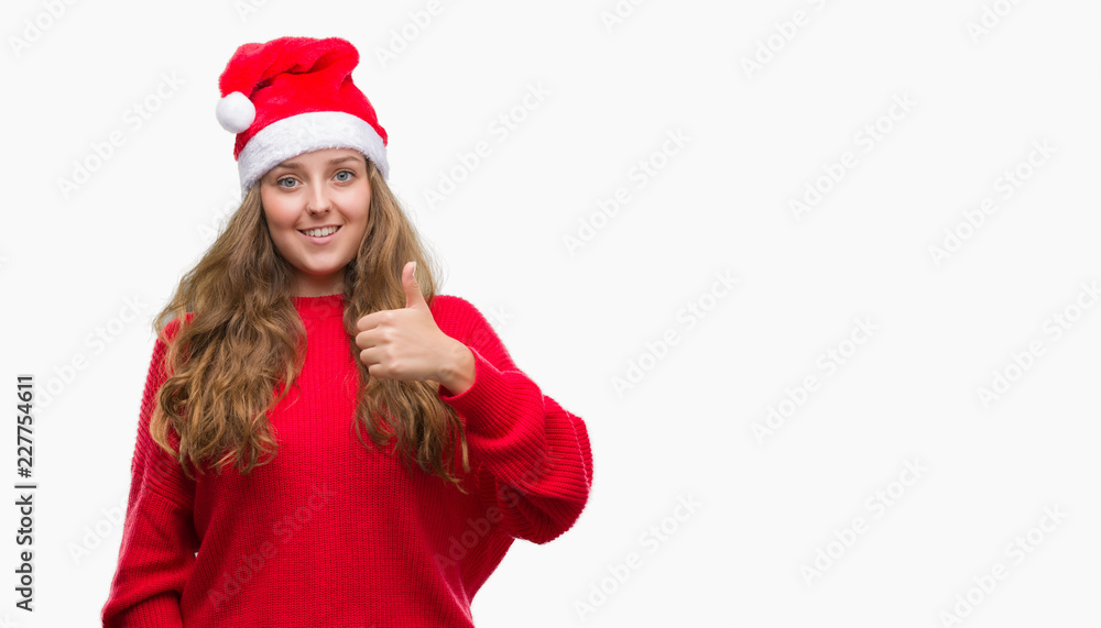 Young blonde woman wearing santa claus hat happy with big smile doing ok sign, thumb up with fingers, excellent sign Young blonde woman wearing santa claus hat happy with big smile doing ok sign, thumb up with fingers, excellent sign