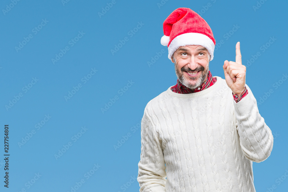Naklejka premium Middle age hoary senior man wearing christmas hat over isolated background pointing finger up with successful idea. Exited and happy. Number one.