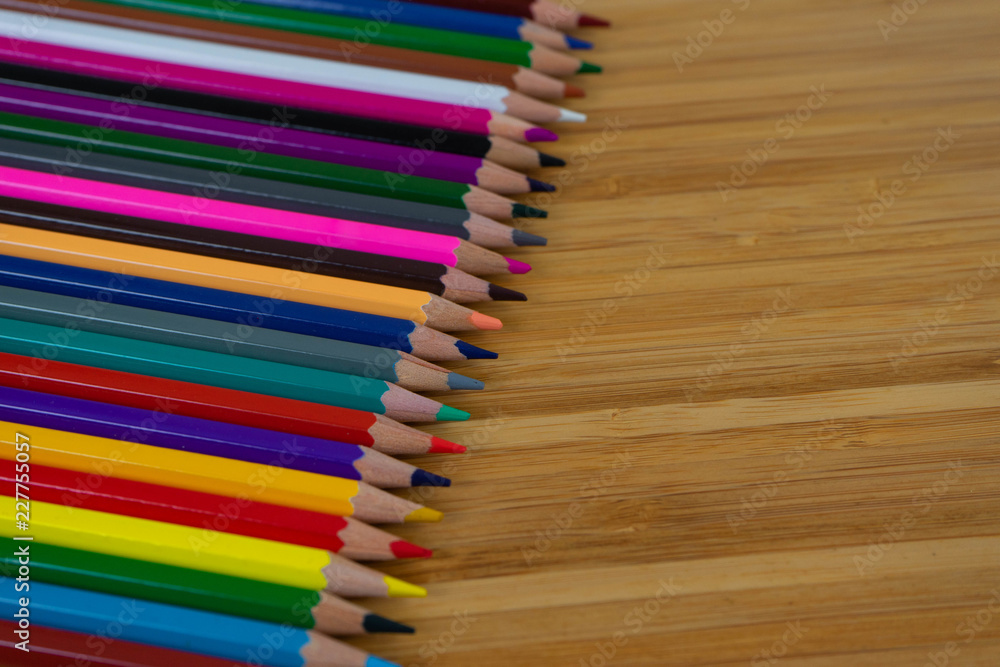 Fototapeta premium Multi-colored pencils lined up in a row and on brown background.