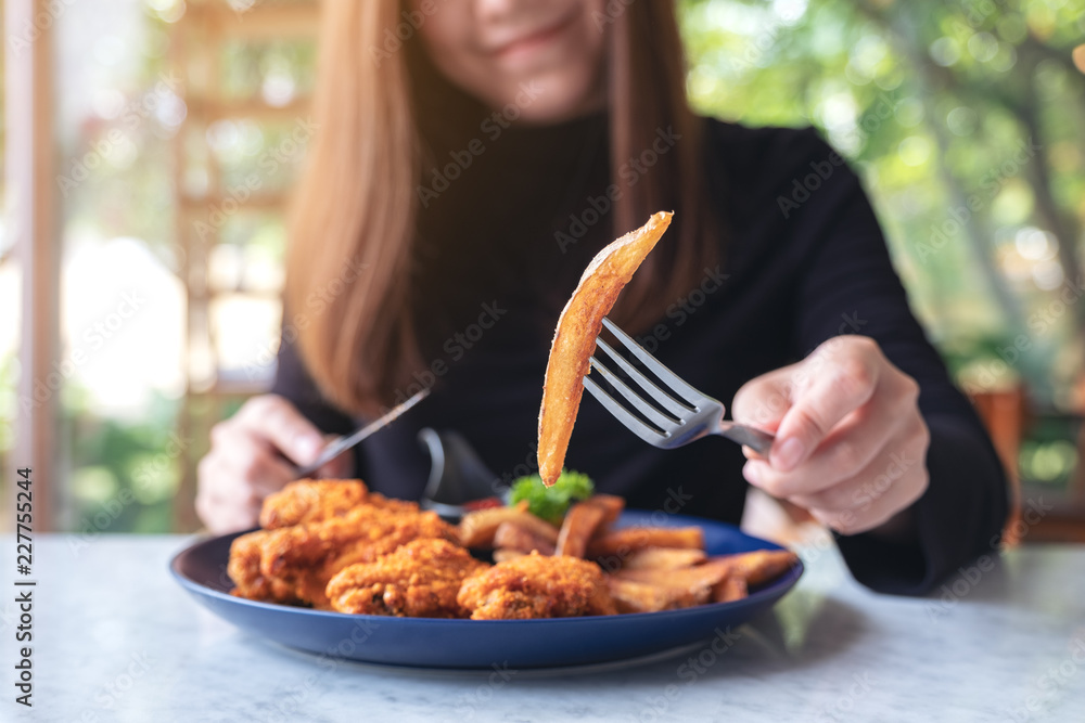 Closeup image of a woman's hand using knife and fork to eat french fries and fried chicken in restaurant Closeup image of a woman's hand using knife and fork to eat french fries and fried chicken in restaurant