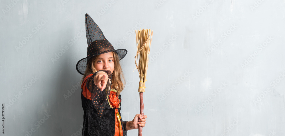 Little girl dressed as a witch and holding a broom for halloween holidays pointing to the front